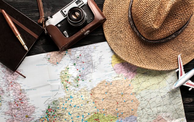 préparatifs de voyage avec appareil photo vintage, carnet, chapeau en paille et carte du monde sur fond bois