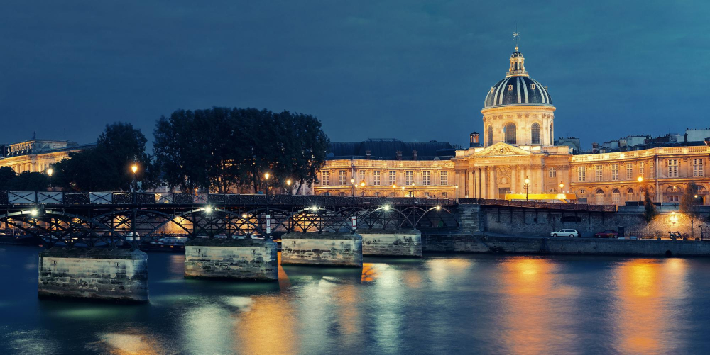 Pont des Arts illuminé la nuit avec la coupole de l'Institut de France en arrière-plan, vue depuis la Seine à Paris