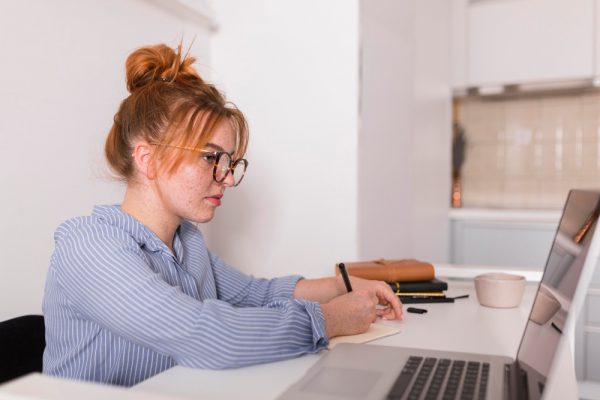 Jeune femme qui prend des notes devant un ordinateur au bureau