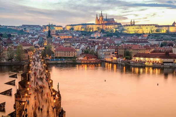 Pont Charles bondé de visiteurs avec le château de Prague et la cathédrale Saint-Guy illuminés au crépuscule, reflets sur la Vltava