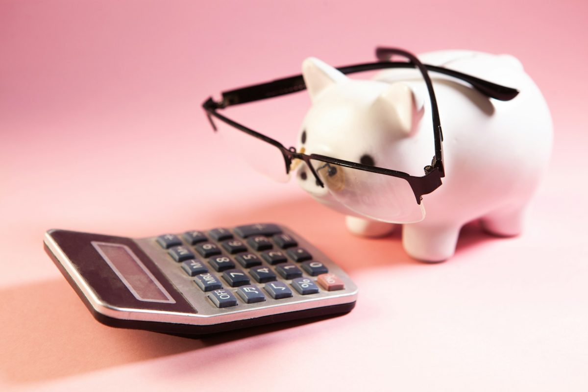 tirelire avec un cochon qui porte des lunettes et regarde une calculatrice pour mesurer des promotions de voyage