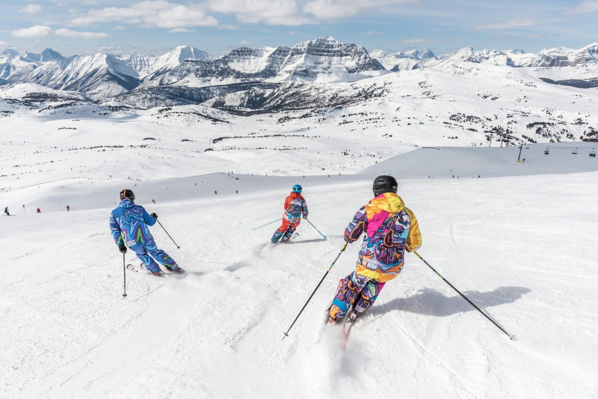 3 skieurs vu de dos dévalant une piste de ski lors de vacances au ski