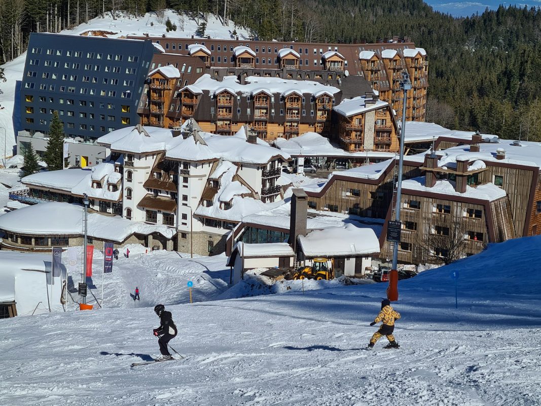 Parent et enfant skiant sur une piste devant des résidences au pied des pistes