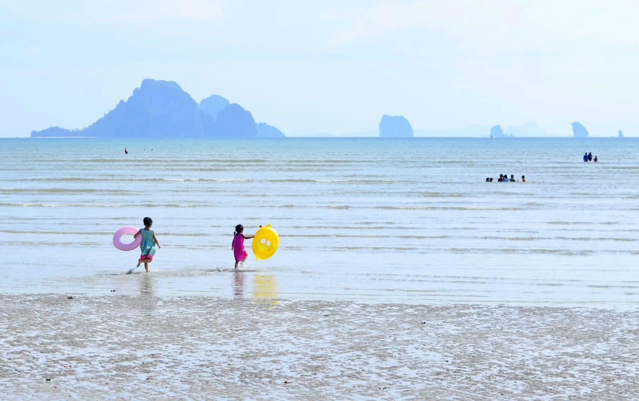 Deux enfants courent vers la mer avec leurs bouées sur une plage de la mer d'Andaman, face aux pitons calcaires, en Thaïlande